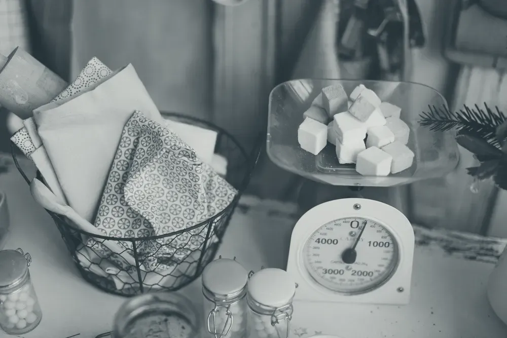 Balança de cozinha analógica com mostrador em gramas, pesando cubos de marshmallow.