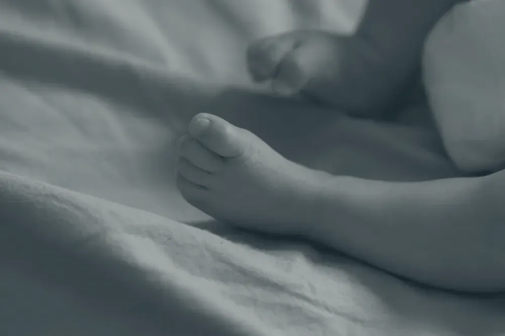Pezinho de bebê em foco, apoiado sobre um cobertor macio em tom quente.