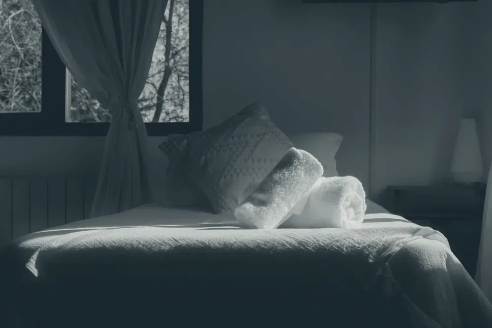 Quarto aconchegante com cama arrumada iluminada pela luz suave da manhã entrando pela janela.